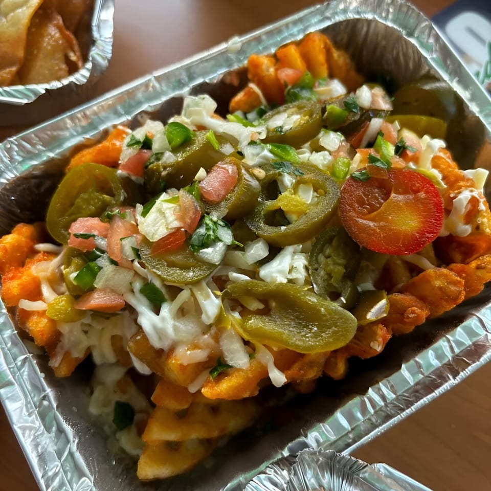 Taco Verde's waffle fries topped with jalapeños, pico de gallo, and sour cream in a foil container.