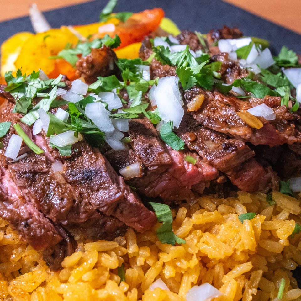 Taco Verde's Mexican dish with sliced steak, yellow rice, cilantro, and diced onions.